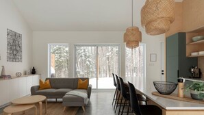A modern kitchen with a dining area, large windows, and a cozy seating area. - Woodland Cocoon | Fireplace • 15min Tremblant (Les Laurentides Regional County Municipality)