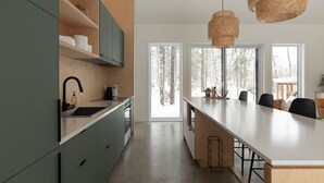 A modern kitchen with a central island, built-in cabinets, and a large window providing a view of the outdoors. - Woodland Cocoon | Fireplace • 15min Tremblant (Les Laurentides Regional County Municipality)
