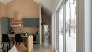 A modern kitchen with a central island, bar stools, and a dining area with a sofa. - Woodland Cocoon | Fireplace • 15min Tremblant (Les Laurentides Regional County Municipality)