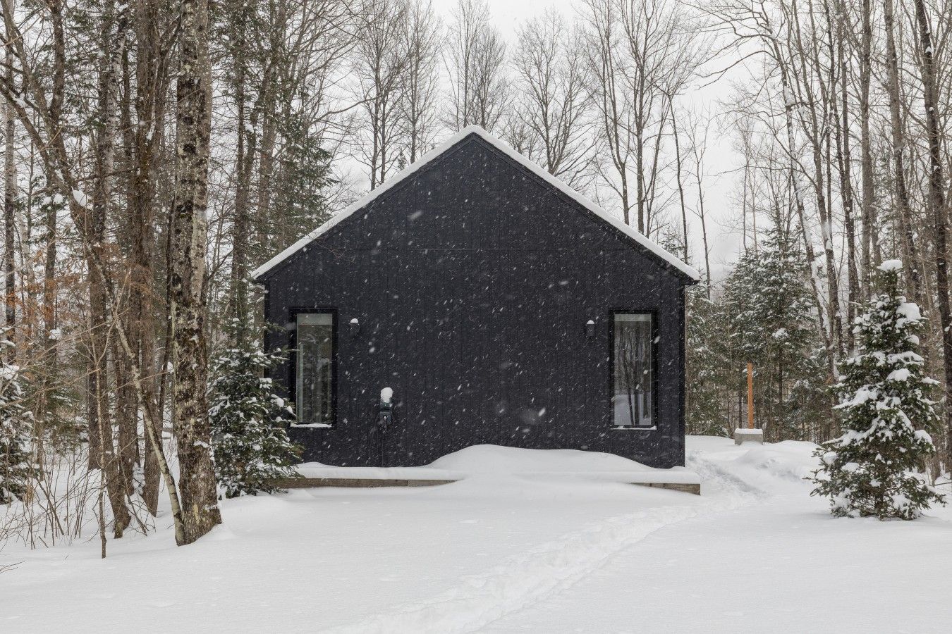 Ein mit Schnee bedecktes Blockhaus mit einem steilen Dach, umgeben von Bäumen und verschneitem Gelände.