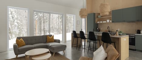 Un espacio habitable moderno con sofá, sillas, una mesita y una cocina con taburetes de bar.
