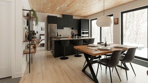 A modern kitchen with a wooden ceiling, a dining area with a wooden table and chairs, and a view of trees through large windows.