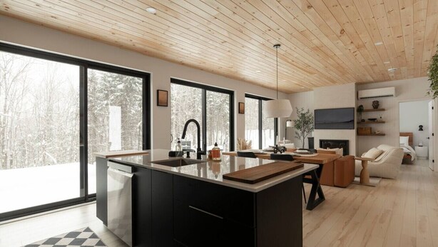 A modern kitchen with a large island, black cabinetry, and a wooden ceiling.