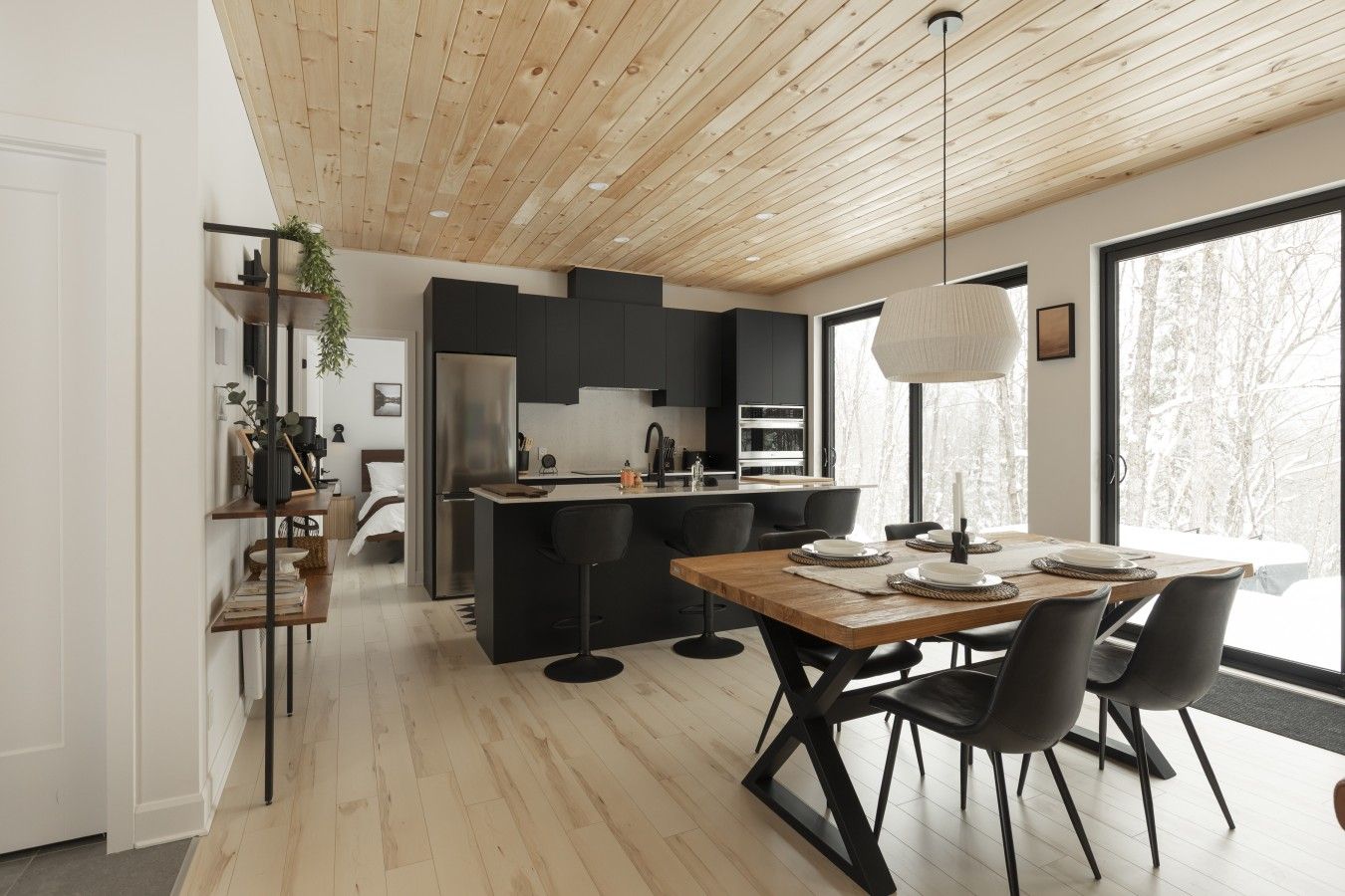 A modern kitchen with a central island, black cabinetry, and a dining area with a wooden table and chairs.