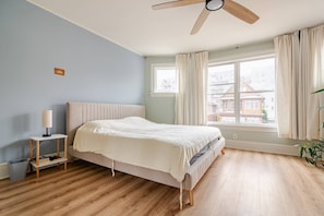 A bedroom with a bed, a bedside table with a lamp, a ceiling fan, a window with curtains, and a view of buildings outside. - Stylish 4-bdrm house in Kensington with parking and backyard available for May (Brooklyn)