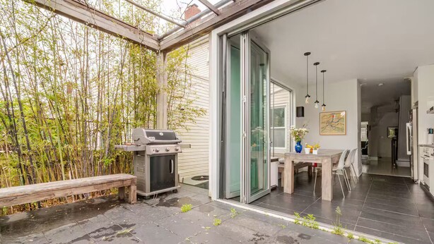A patio with a grill, a table, and chairs, surrounded by bamboo plants. - Spacious, artful 4-bedroom house in Brooklyn with lush backyard, parking, A/C (Brooklyn)