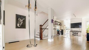 A spacious living room with hardwood floors, a staircase, a bookshelf, and a TV. - Spacious, artful 4-bedroom house in Brooklyn with lush backyard, parking, A/C (Brooklyn)