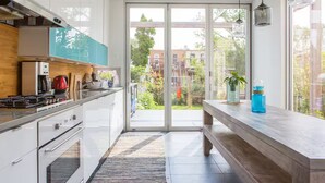 A modern kitchen with white cabinets, a gas stove, and a large sliding glass door leading to a balcony. - Spacious, artful 4-bedroom house in Brooklyn with lush backyard, parking, A/C (Brooklyn)