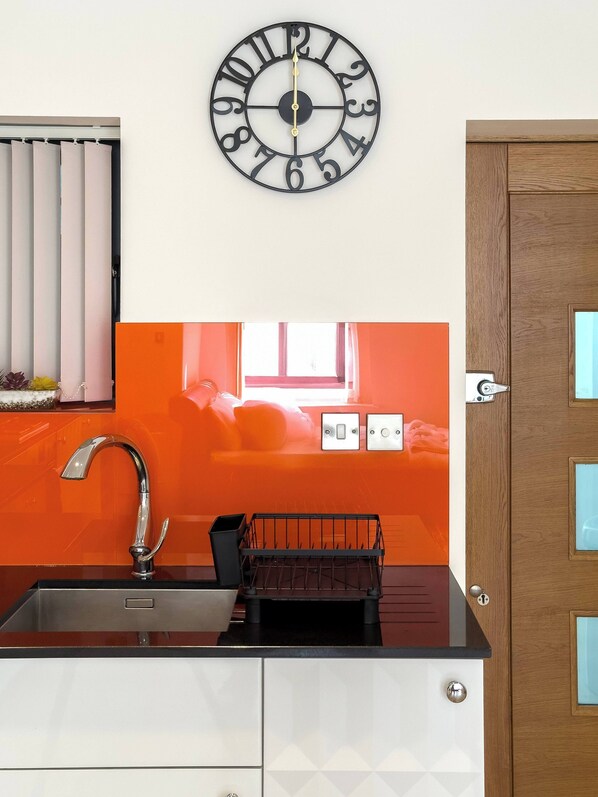 A kitchen with a modern faucet, a black clock, and a wooden door.