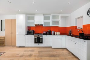 A modern kitchen with white cabinetry, a black stove, and a red accent wall.