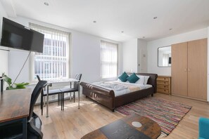A modern bedroom with a bed, a desk, a chair, a TV, and a wardrobe.