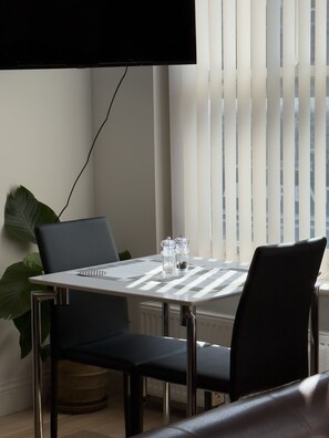 A dining area with a table, chairs, a television mounted on the wall, and a window with blinds.
