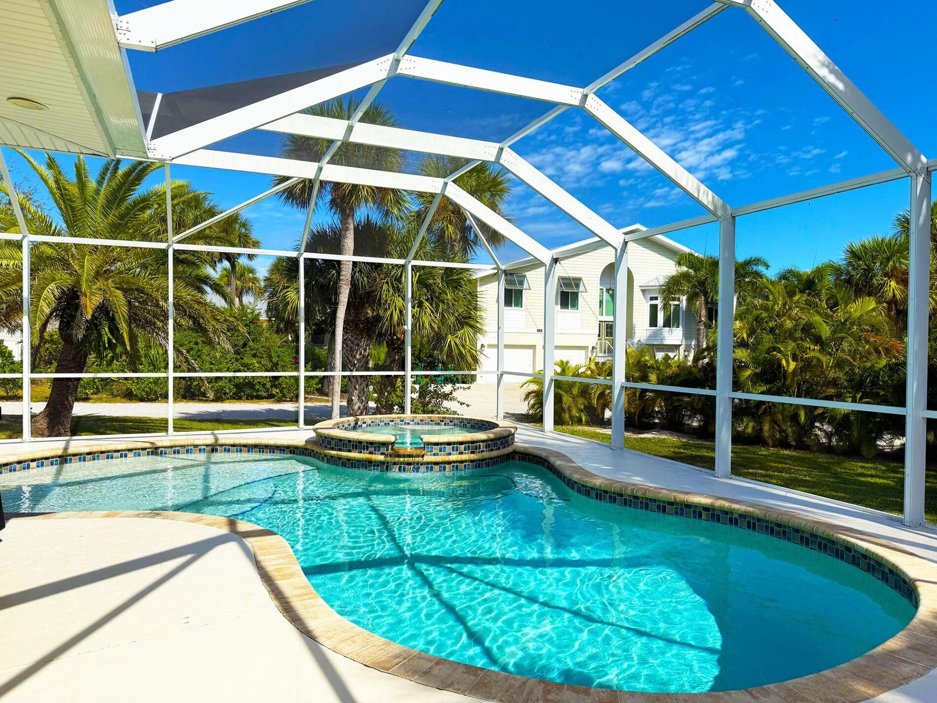Une piscine couverte avec un jacuzzi, entourée de palmiers et bordée d’un bâtiment blanc en arrière-plan.