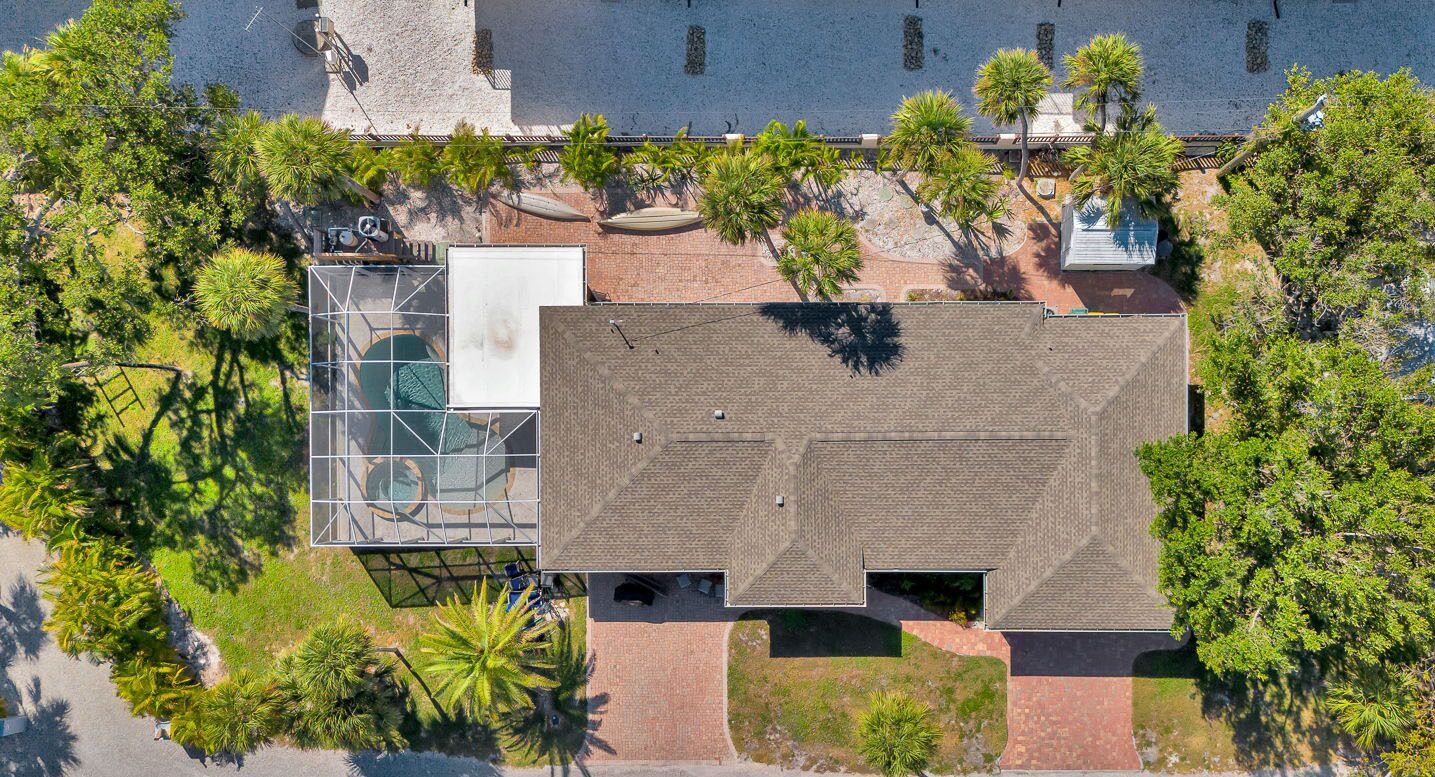 An aerial view of a building with a flat roof, surrounded by trees and a body of water.