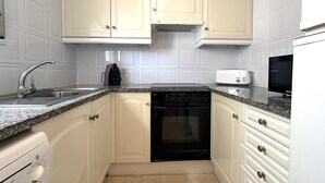 Una cocina con muebles blancos, lavavajillas negro, microondas y encimera de granito.