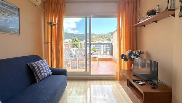 Una sala de estar con sofá, televisor y un balcón con mesa y sillas.