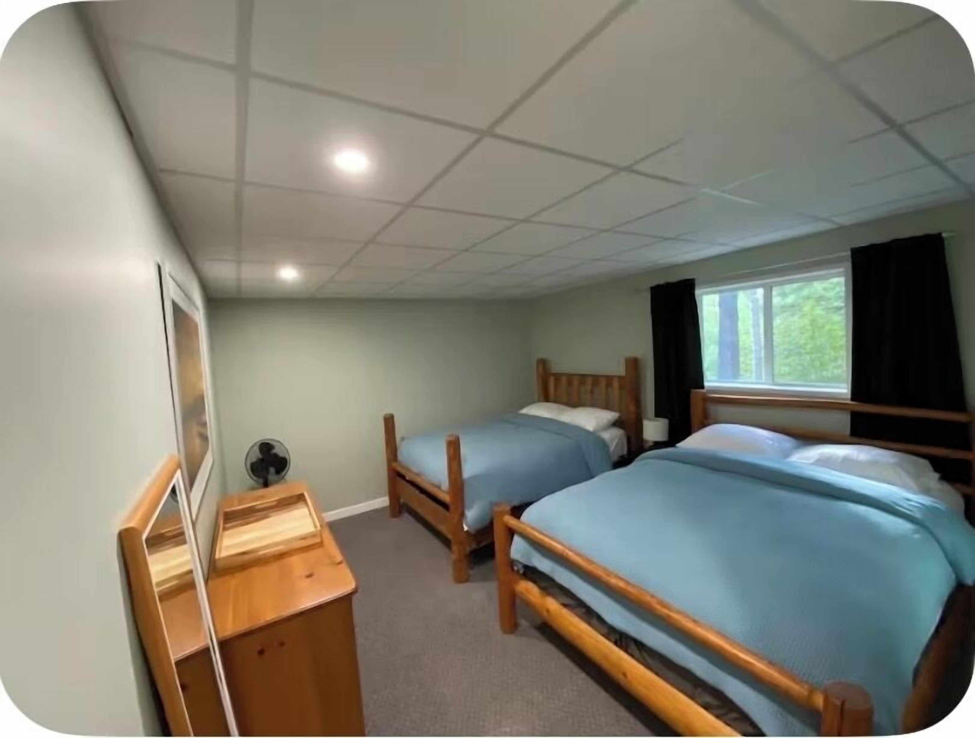Une chambre avec deux lits, un bureau, une chaise, une fenêtre avec des rideaux et un ventilateur de plafond.