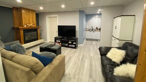 Ein Wohnzimmer mit Kamin, Fernseher und Küchenzeile mit Schränken und Kühlschrank.
