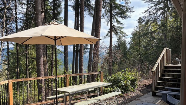 Ein Picknickbereich mit Tisch und Bank, umgeben von einer Holzterrasse und einem Wald im Hintergrund.