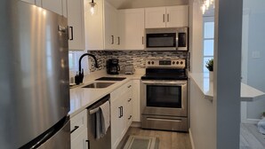 A compact kitchen with stainless steel appliances, white cabinetry, and a tiled backsplash.