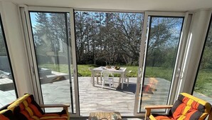 Een zonnig terras met een houten tafel voor vier personen, omringd door twee gestreepte banken.