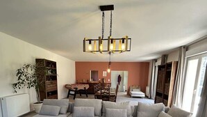 Een ruime woonkamer met een grote hoekbank, een eethoek op de achtergrond en een moderne kroonluchter.