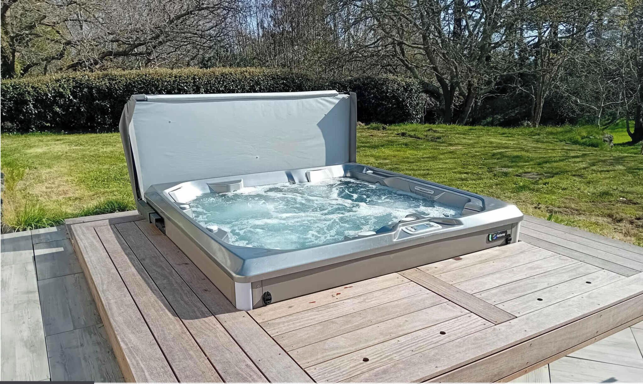 A hot tub on an outdoor wooden deck with a hedge and trees in the background.