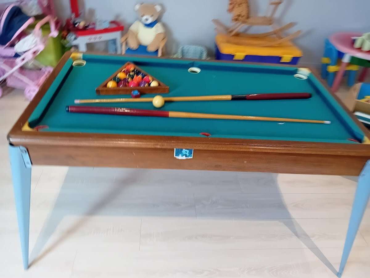 A pool table with pool cues, a cue ball, and a triangle rack of billiard balls.