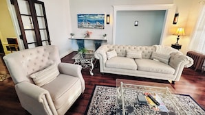 A living room with a beige armchair, a sofa, a glass coffee table, and a patterned rug. -  Elmwood Village home (Buffalo)