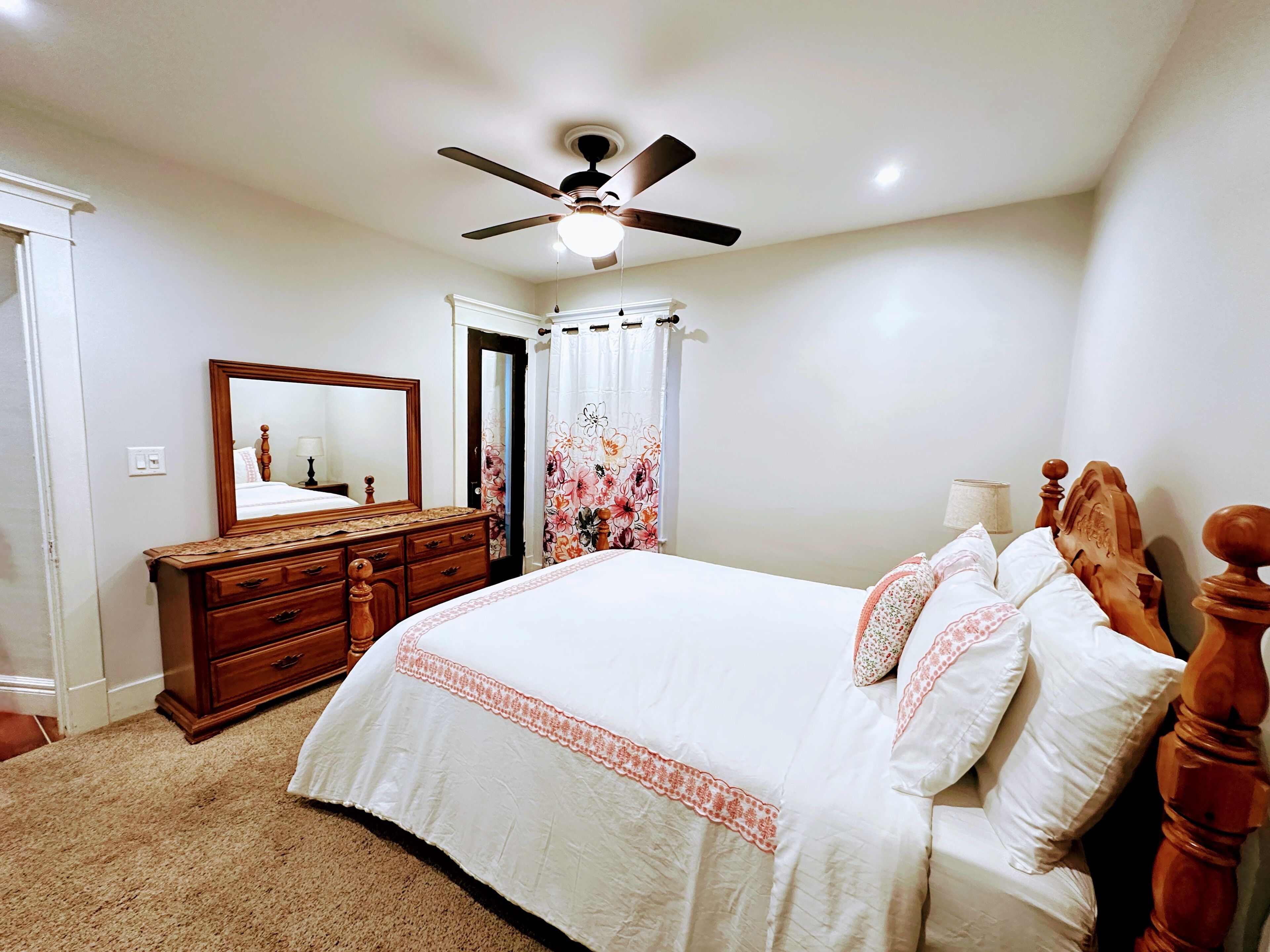 A bedroom with a bed, a dresser, a ceiling fan, and a mirror.
