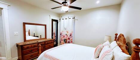 A bedroom with a bed, a dresser, a ceiling fan, and a mirror.
