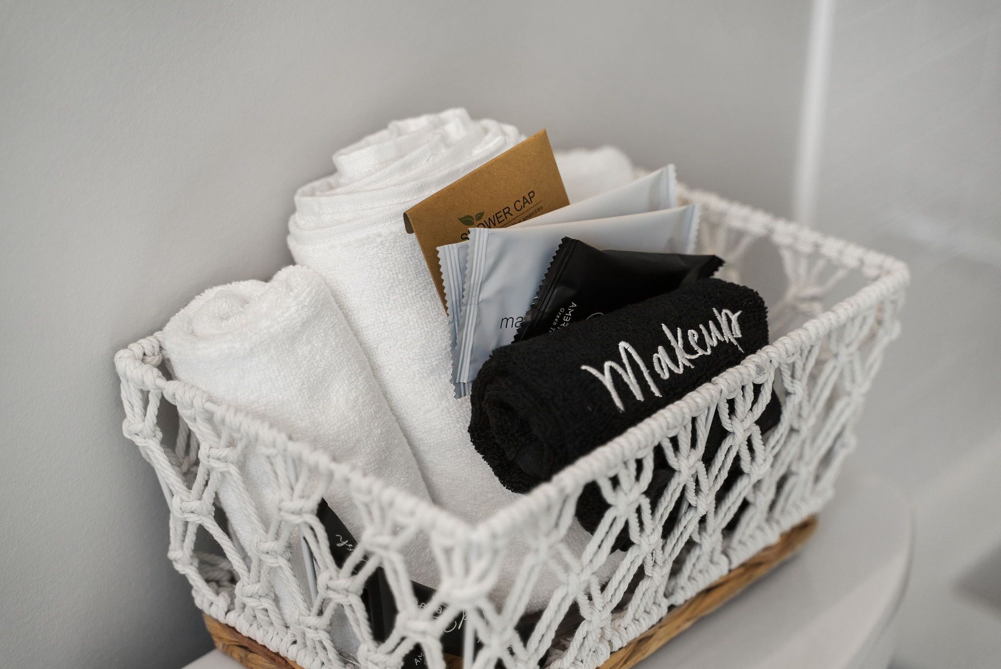 A white macrame basket containing folded towels and a black towel with "Makeover" written on it.