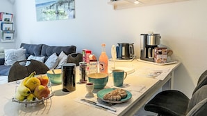 A modern kitchen with a dining table set for breakfast, including fruits, coffee, and pastries.