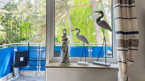 A room with a view of trees through a window, a birdcage, and a railing.