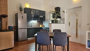 A compact kitchen with a refrigerator, microwave, and cabinets, a dining table with chairs, and a white door with a decorative arch. - Casa Oliva Kim Marie /w Garden, Medulin, Croatia (Medulin)
