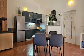 Una cocina compacta con refrigerador, microondas y armarios, una mesa de comedor con sillas, y una puerta blanca con un arco decorativo.