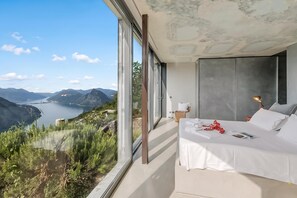 A bedroom with a large window overlooking a mountainous landscape and a lake. - Villa Skyline - Pool - Lakeview - Privacy, Lugano, Switzerland (Lugano)