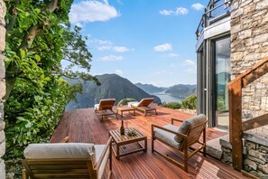 A wooden deck with outdoor furniture overlooking a mountainous landscape and a body of water. - Villa Skyline - Pool - Lakeview - Privacy, Lugano, Switzerland (Lugano)