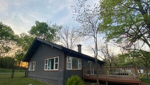 A two-story house with a deck, surrounded by trees and a grassy yard. - Monkey Island Escape sleeps 8, surrounded by nature with views of Grand Lake. (Monkey Island)