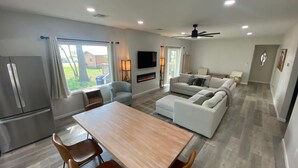 A modern living room with a sofa, a dining table, and a kitchen area with a refrigerator. - Monkey Island Escape sleeps 8, surrounded by nature with views of Grand Lake. (Monkey Island)