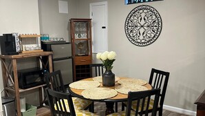 A dining area with a round wooden table, four chairs with yellow and white patterned cushions, a vase with white flowers, a decorative wall piece, and a 'WELCOME' sign. - Home away from home with WiFi and AC in delightful Parkville (Parkville)