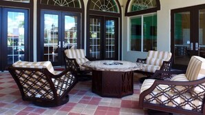 A covered patio with a round table and four wicker chairs, large arched windows, and a ceiling fan. - Near Disney & Supermarket Amazing Home with Pool (Kissimmee)
