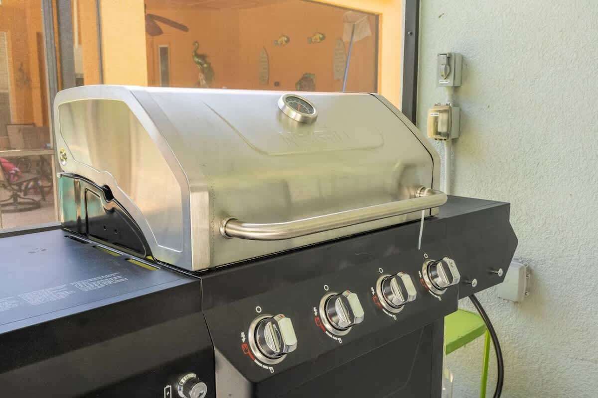 Un barbecue en acier inoxydable doté d’un panneau de commande, placé contre un mur près d’une fenêtre.