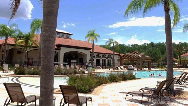 A pool area with lounge chairs, palm trees, and a building with a red roof. - Near Disney & Supermarket Amazing Home with Pool (Kissimmee)