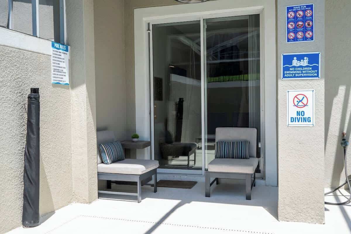 A poolside area with lounge chairs, a glass door entrance, and safety signs including 'No Diving' and 'No Children Swimming Without Adult Supervision'.