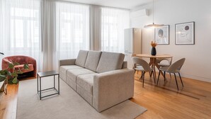 A modern living room with a sofa, a small table, and chairs. There is a dining table with chairs, a plant, and artwork on the wall. - GuestReady - Joy Apartments - C (Porto)
