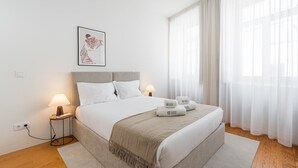 A neatly arranged hotel room with a bed, bedside lamps, a framed artwork, and a window with sheer curtains. - GuestReady - Joy Apartments - C (Porto)