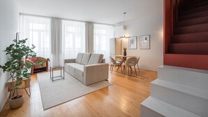 A modern living room with a sofa, dining table, and chairs, a staircase, and a potted plant. - GuestReady - Joy Apartments - C (Porto)