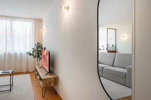 Una sala de estar moderna con un sofá gris, una mesita de madera con una planta y un espejo grande en la pared.