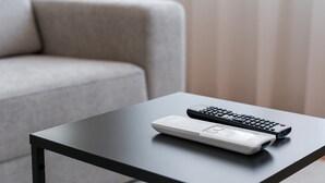 A remote control and a white device on a black table in a room with a grey sofa.